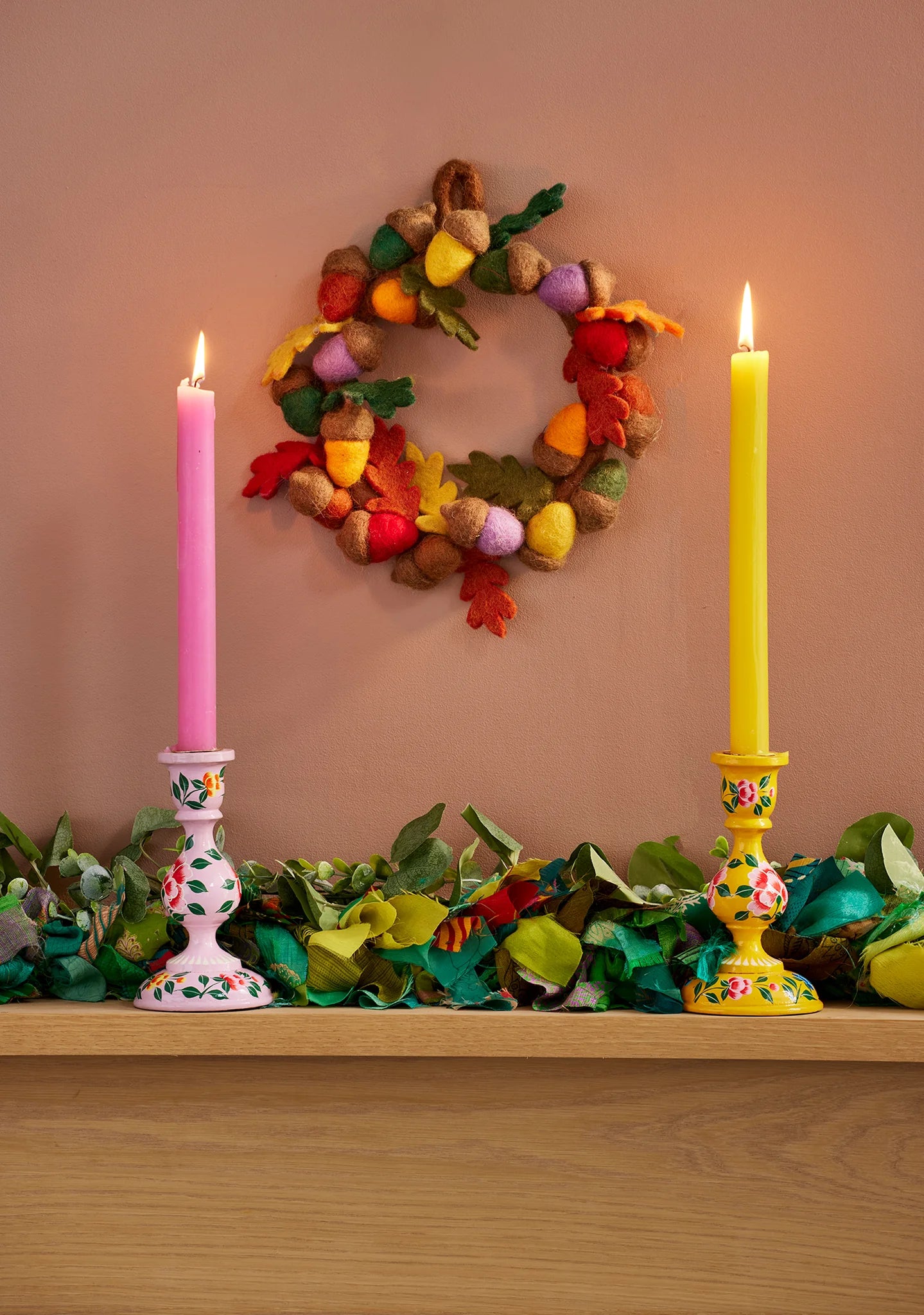 Decorative shelf with colorful candles, garland, and wreath against a beige wall.