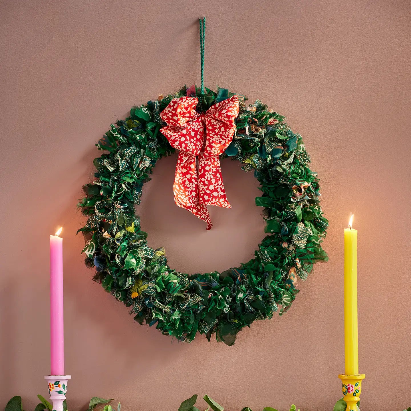 Green wreath with a red bow, pink and yellow candles on a beige background