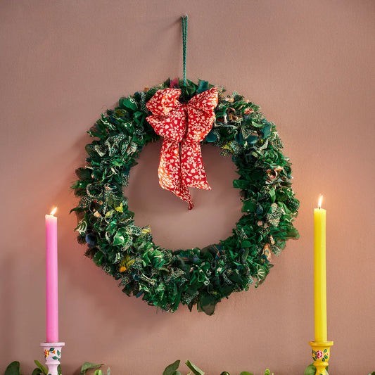 Green wreath with a red bow, pink and yellow candles on a beige background