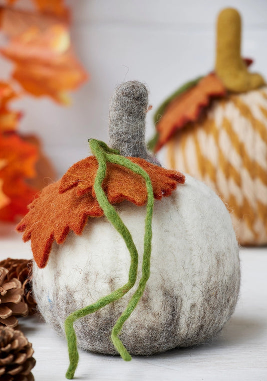 Felted pumpkin decoration with orange leaf and green stem on a blurred background
