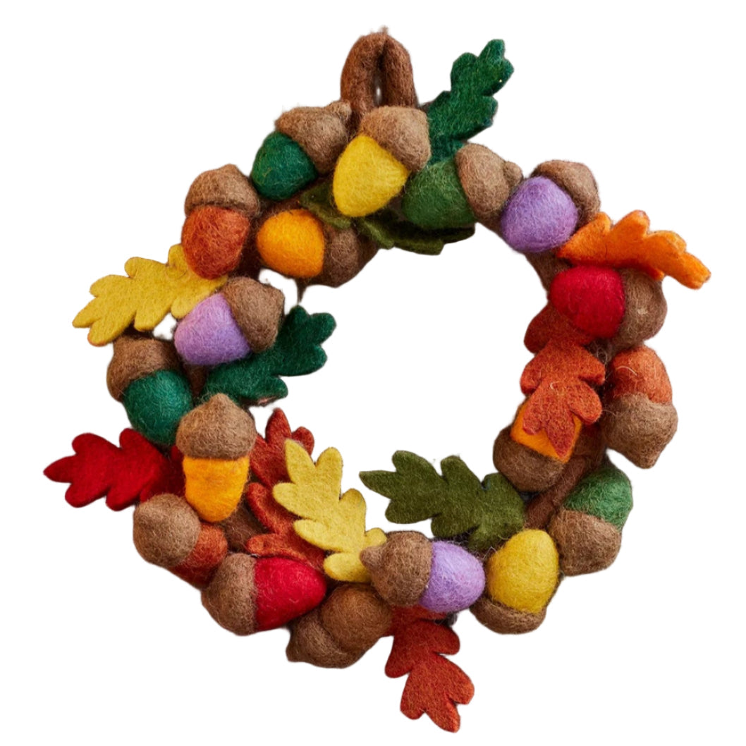 Decorative wreath with colorful leaves and acorns above three polka-dotted mushrooms on a wooden surface.