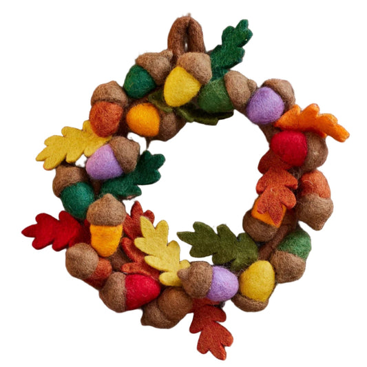 Decorative wreath with colorful leaves and acorns above three polka-dotted mushrooms on a wooden surface.